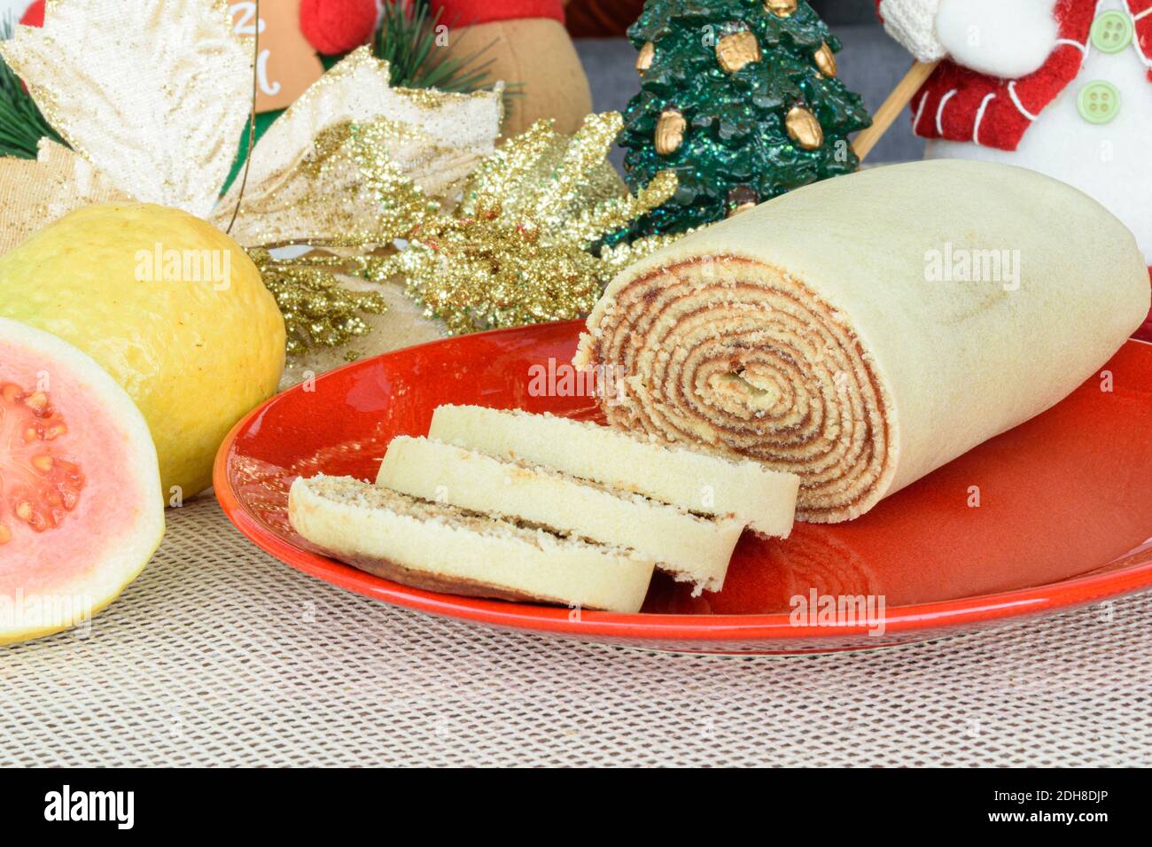 Bolo de rolo (Kuchenrolle) neben Guavas und Weihnachtsdekoration. Stockfoto