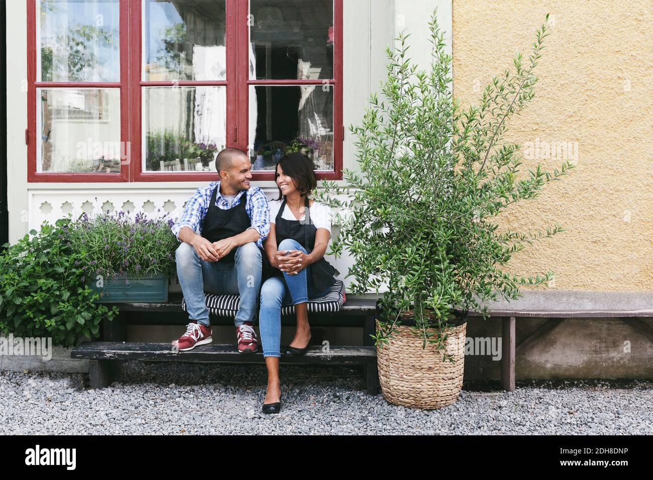 Lächelnde Besitzer sitzen auf der Bank gegen das Fenster vor dem Café Stockfoto