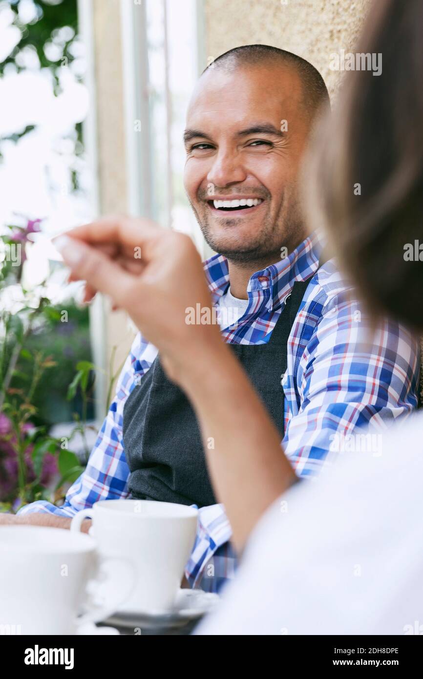 Lächelnder Mann mit einer Kollegin, die vor dem Café am Tisch sitzt Stockfoto