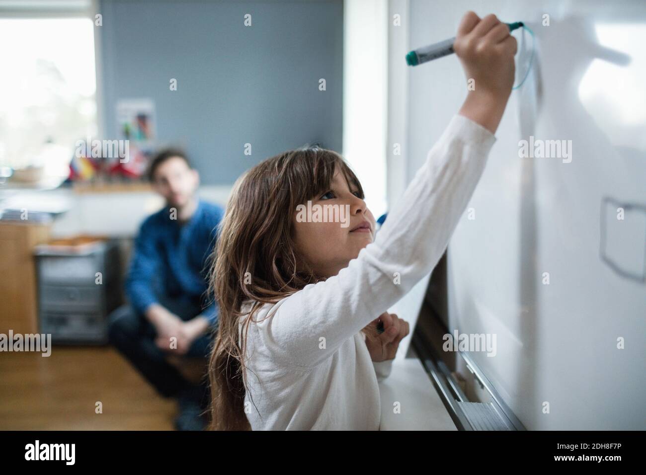 Zuversichtlich Mädchen Zeichnung auf Tafel, während Lehrer im Hintergrund sitzen Stockfoto