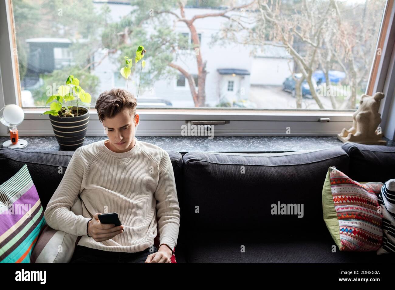 Mann mit Smartphone, während er auf dem Sofa sitzt bei New Zu Hause Stockfoto