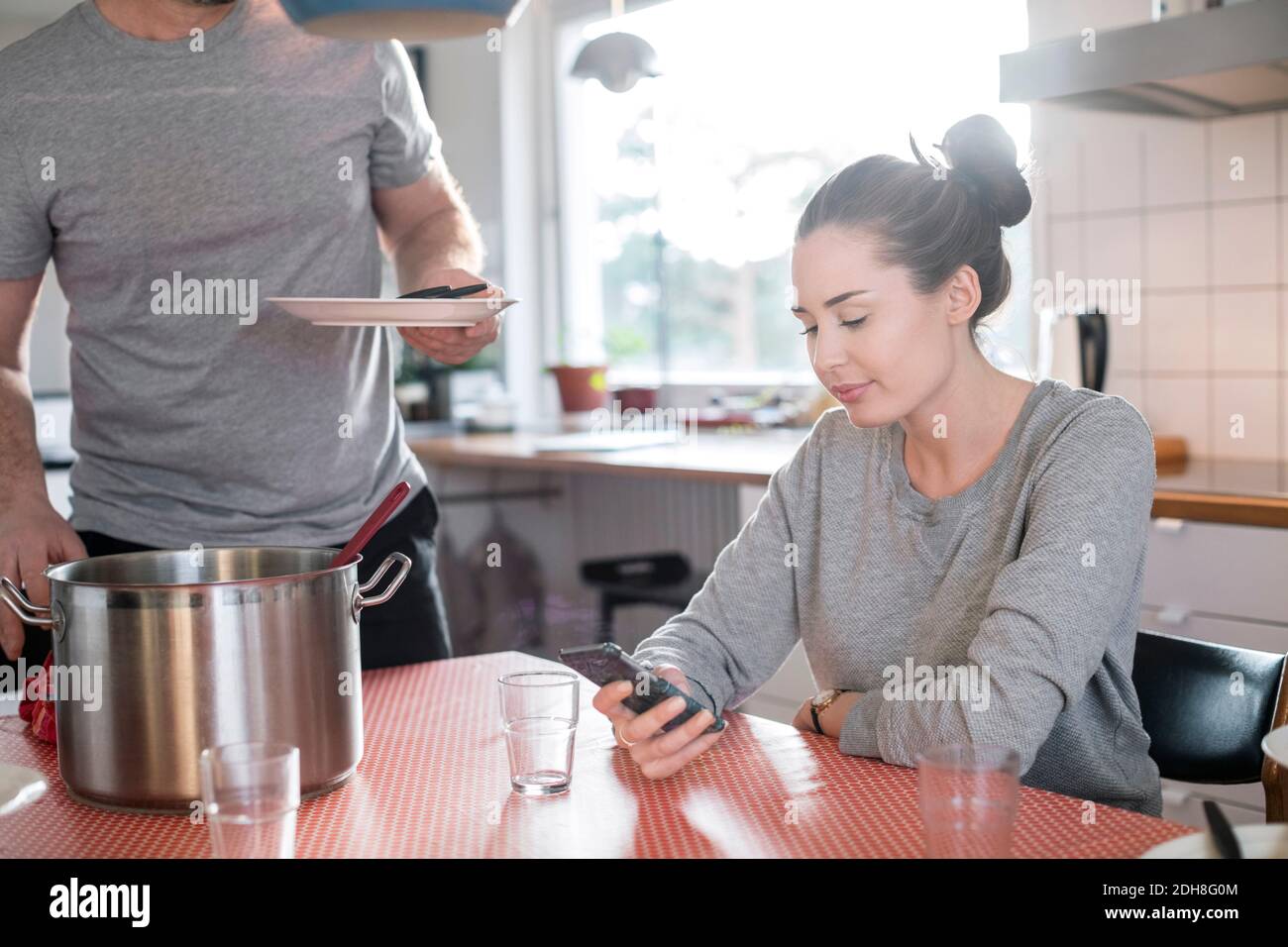 Mittelteil des Vaters hält Platte, während Tochter Smartphone verwenden Am Esstisch in der Küche Stockfoto