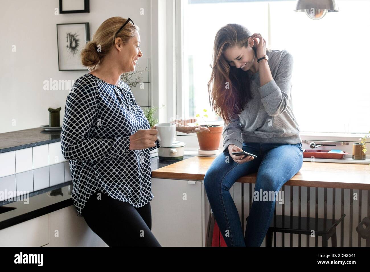 Mutter im Gespräch mit glücklichen Tochter mit Smartphone in der Küche Stockfoto