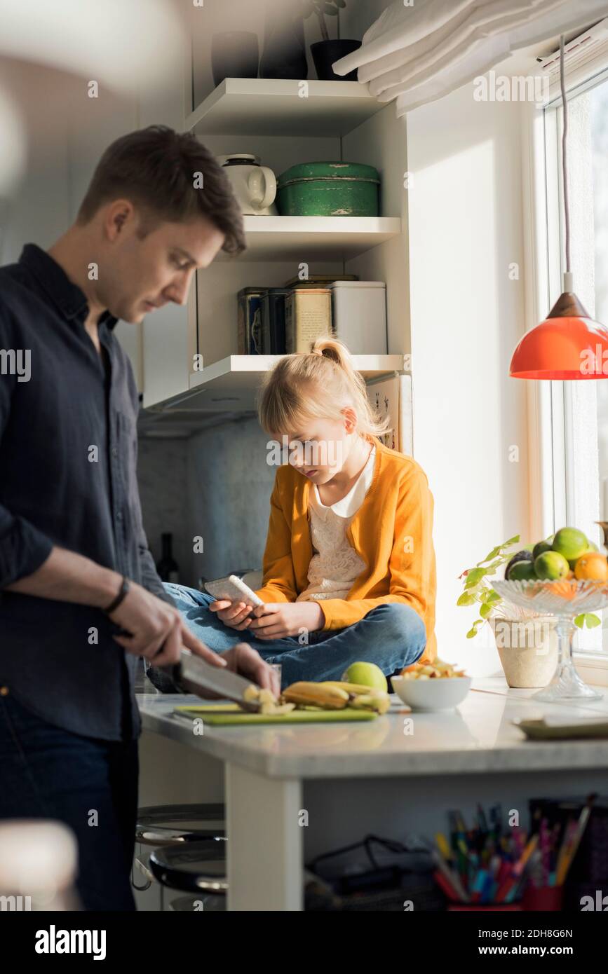 Vater schneiden Früchte weiß Mädchen mit Handy in der Küche Stockfoto