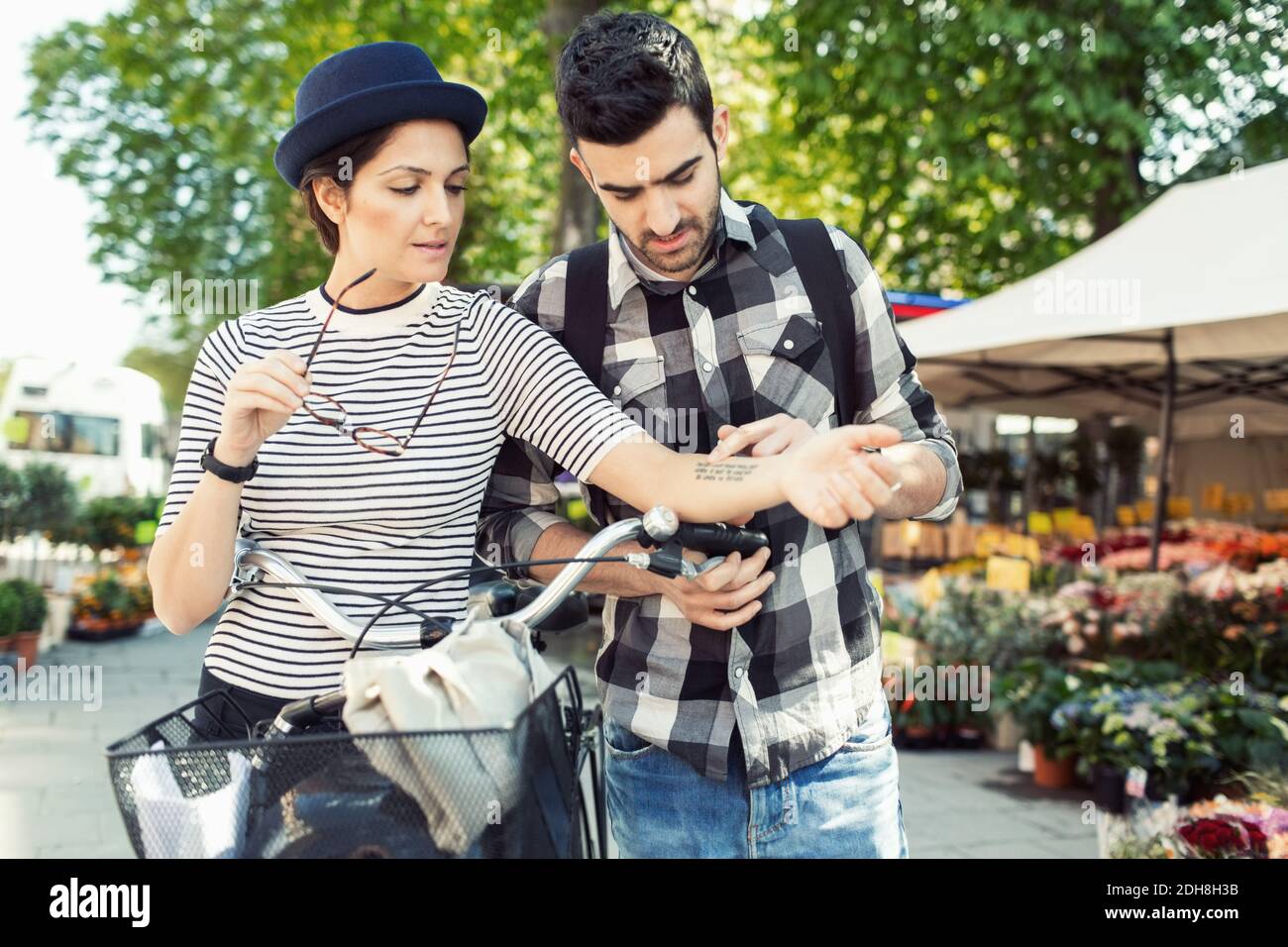 Mann, der Tattoo auf der Hand einer Frau liest, während er bei der Blume steht Kaufen Stockfoto