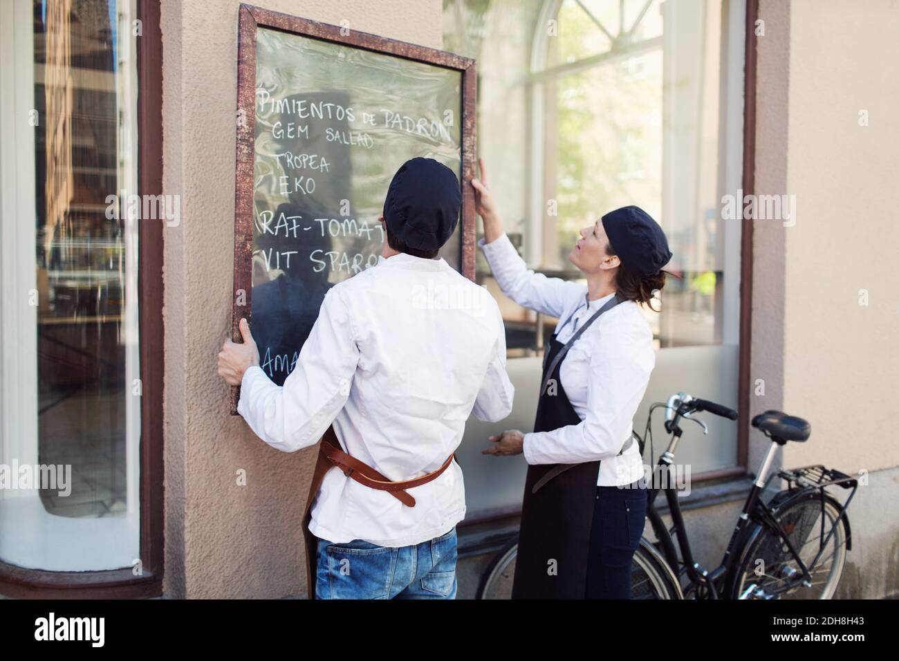 Männliche und weibliche Besitzer, die vor dem Lebensmittelgeschäft eine Tafel an die Wand stellen Speichern Stockfoto