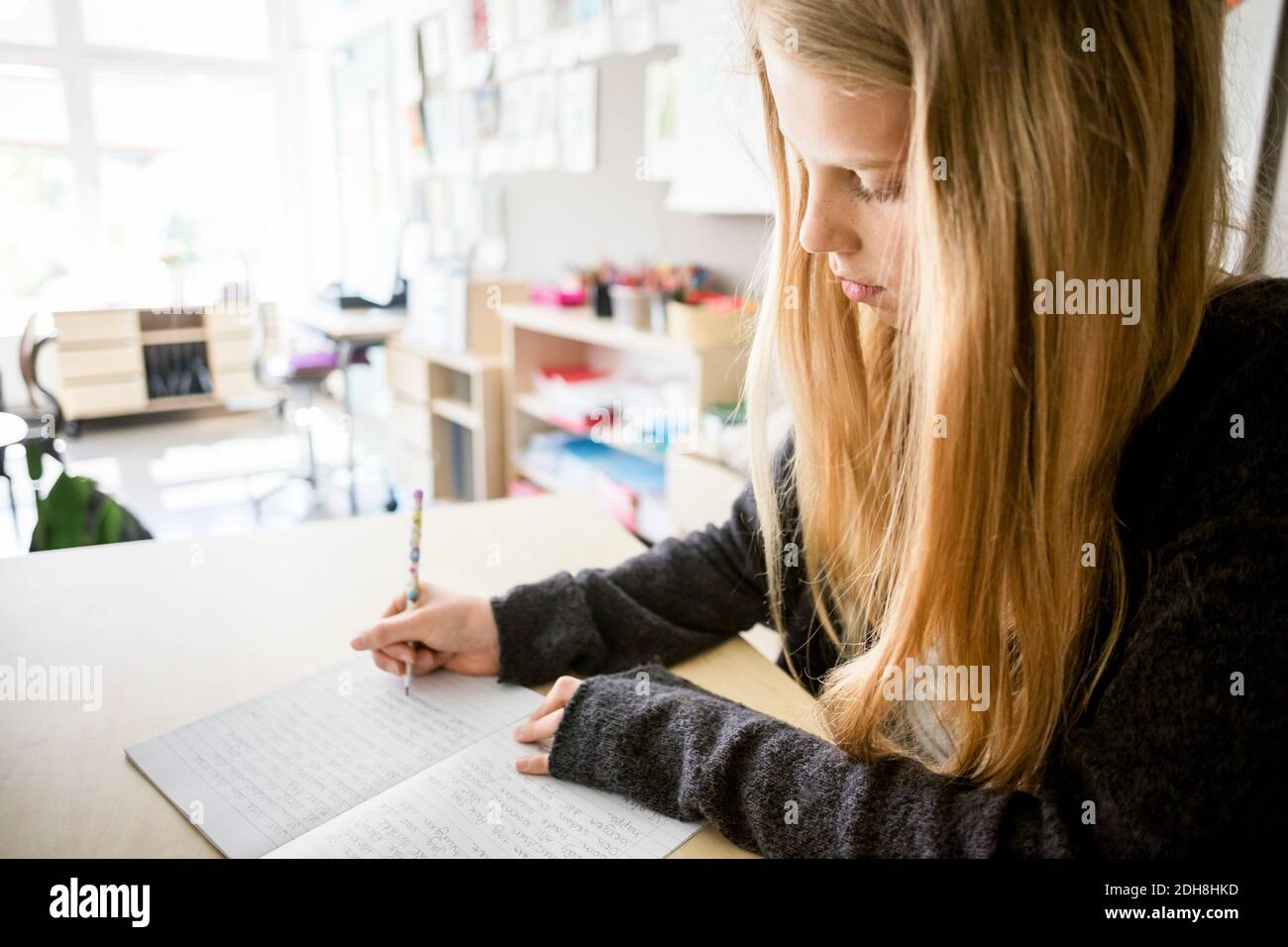 Mädchen, das im Buch auf dem Schreibtisch im Klassenzimmer schreibt Stockfoto