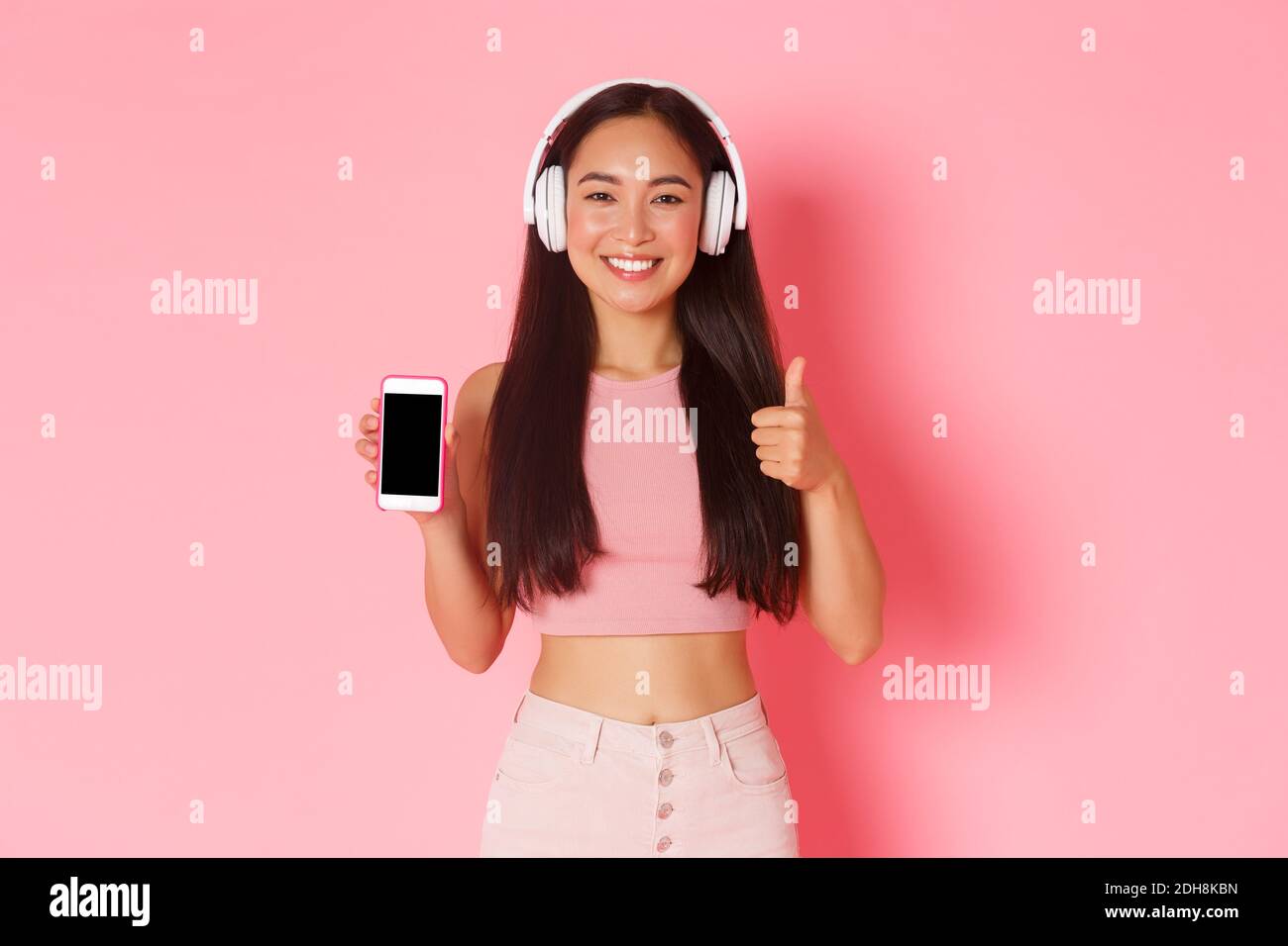 Technologie, Kommunikation und Online Lifestyle Konzept. Zufriedene fröhliche asiatische Mädchen in Kopfhörer, zeigt Smartphone-Display Stockfoto