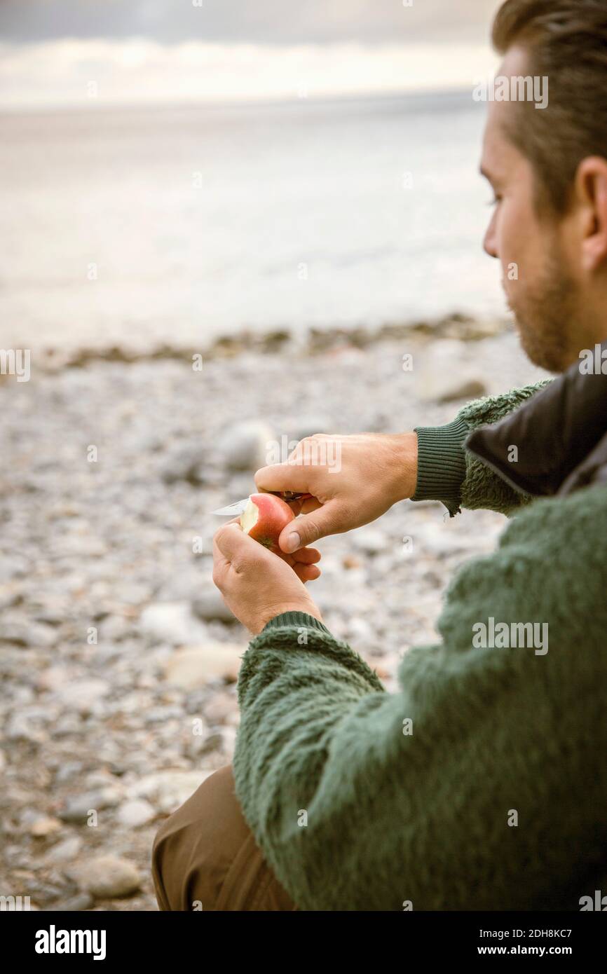 Zugeschnittenes Bild eines Mannes, der am Strand einen Apfel schneidet Stockfoto