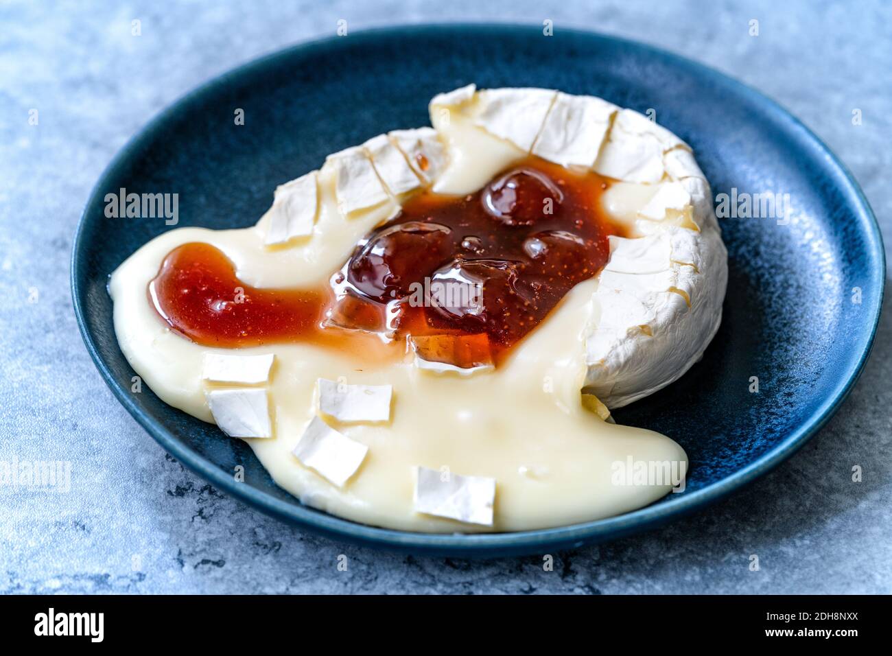 Gebackenes Brie-Käse-Dessert mit Erdbeermarmelade. Marmelade Geschmolzen Camembert. Traditionelles Bio-Dessert. Stockfoto