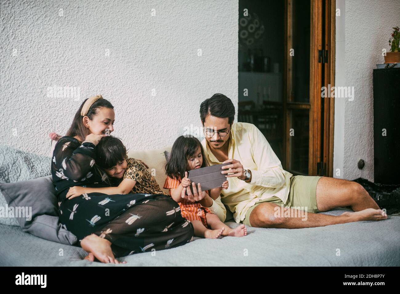 Vater und behinderte Tochter mit digitalen Tablet, während lächelnd Mädchen Mutter zu Hause auf dem Sofa umarmen Stockfoto