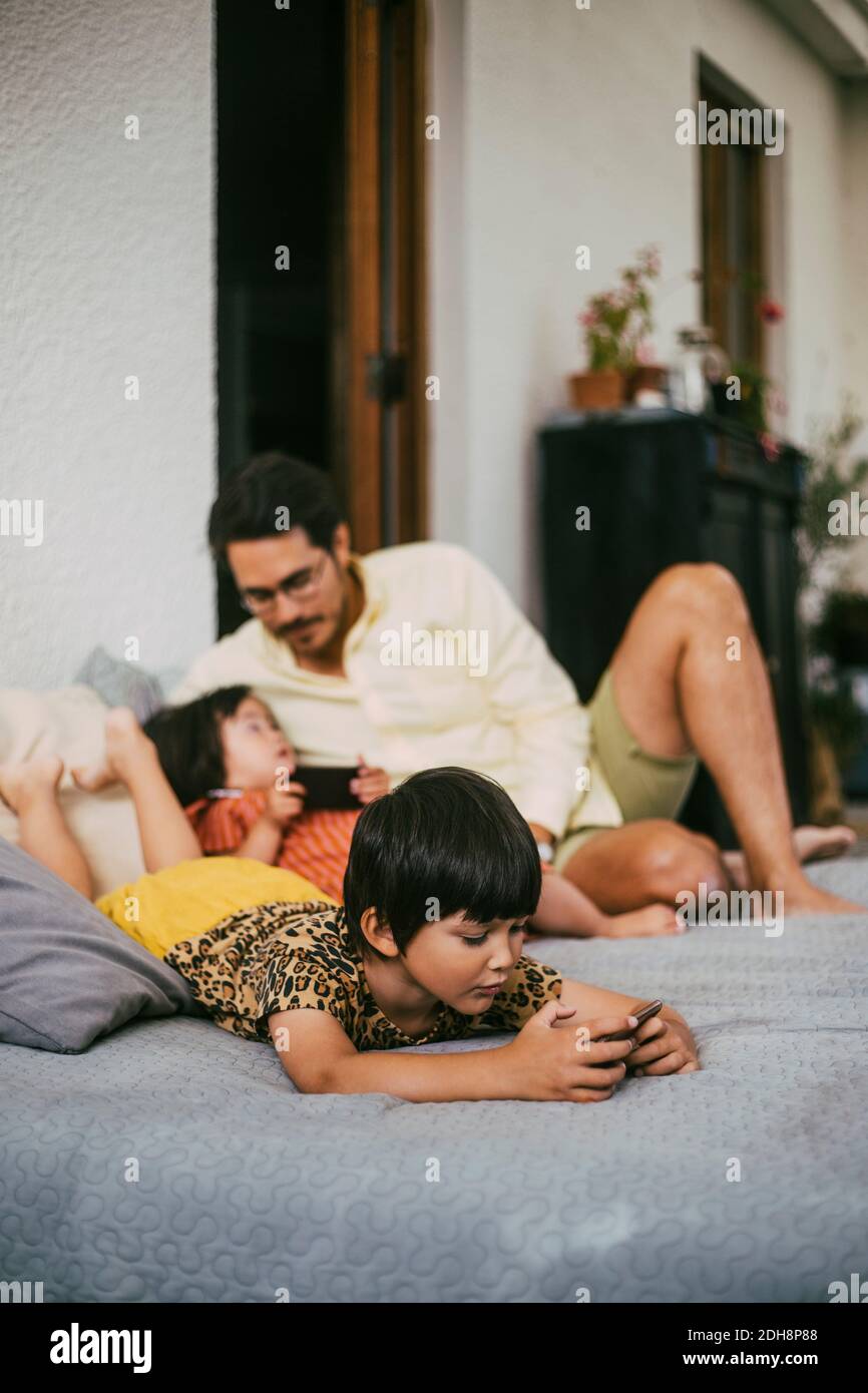 Mädchen mit Smartphone, während Down-Syndrom Mädchen im Gespräch mit Vater auf dem Sofa zu Hause Stockfoto