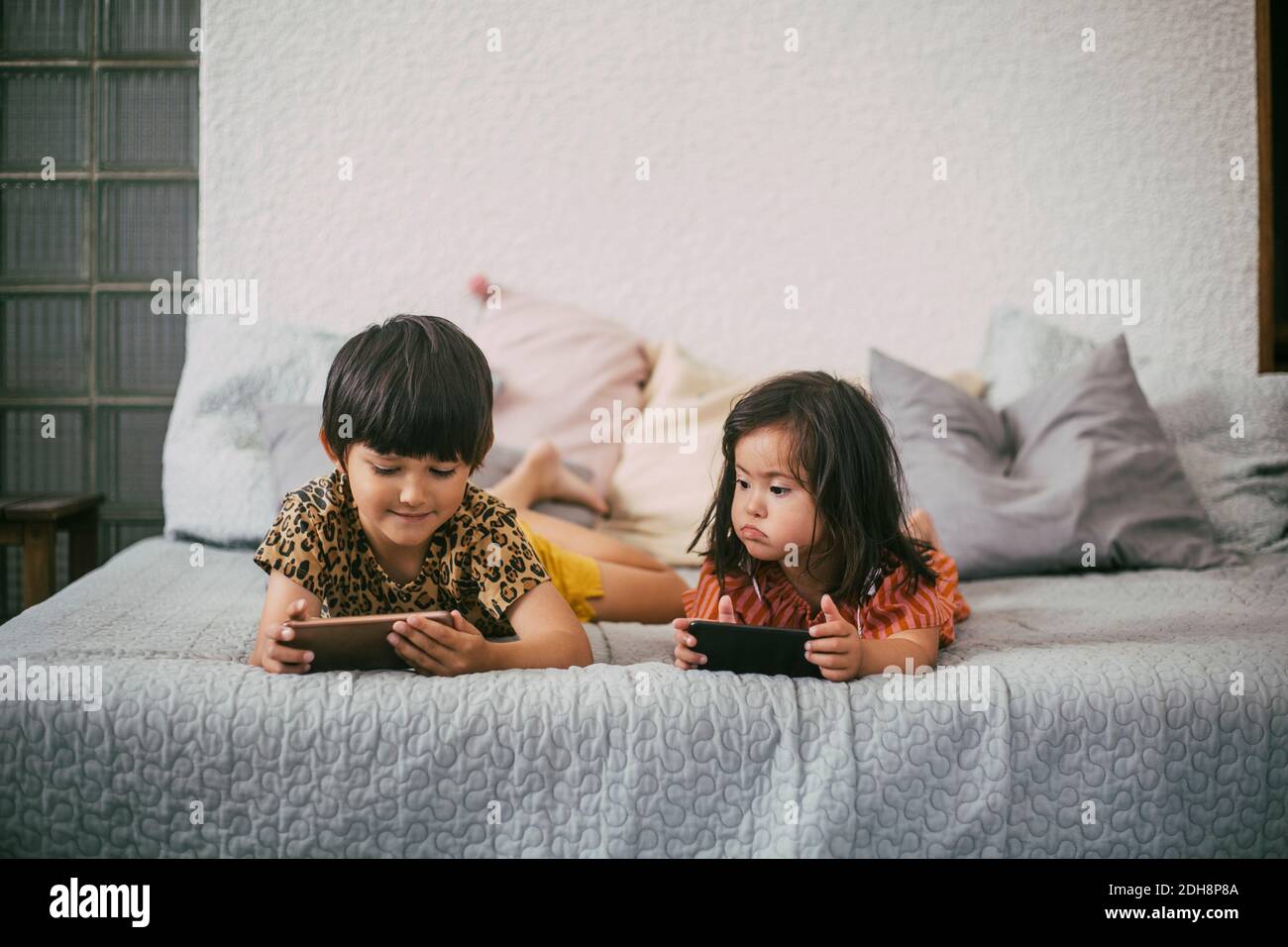 Down-Syndrom Schwester Blick auf Geschwister mit Smartphone, während Liegen auf dem Sofa zu Hause Stockfoto