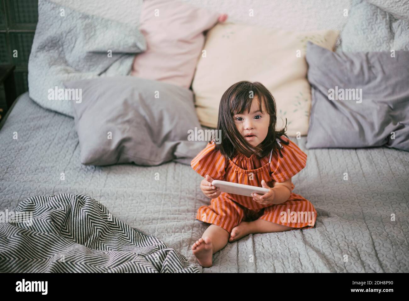 Portrait von Down-Syndrom Mädchen mit digitalen Tablet während des Sitzens Auf dem Sofa zu Hause Stockfoto