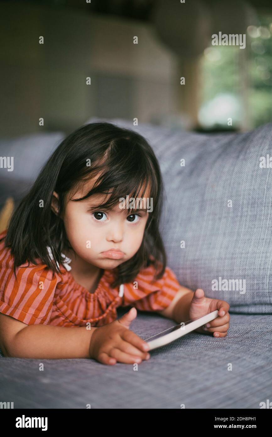Portrait von Down-Syndrom Mädchen mit digitalen Tablet beim Liegen Auf dem Sofa zu Hause Stockfoto