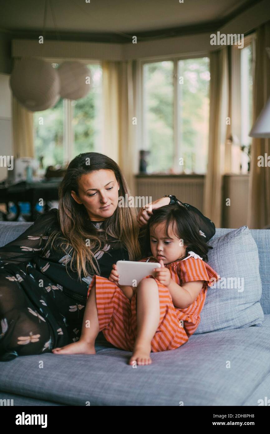 Mutter schaut auf Down-Syndrom Tochter mit Handy, während Sitzen auf einem Sofa im Wohnzimmer Stockfoto