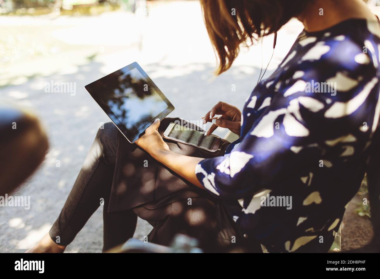 Seitenansicht einer Geschäftsfrau mit Smartphone und digitalem Tablet Während Sie auf der Bank sitzen Stockfoto