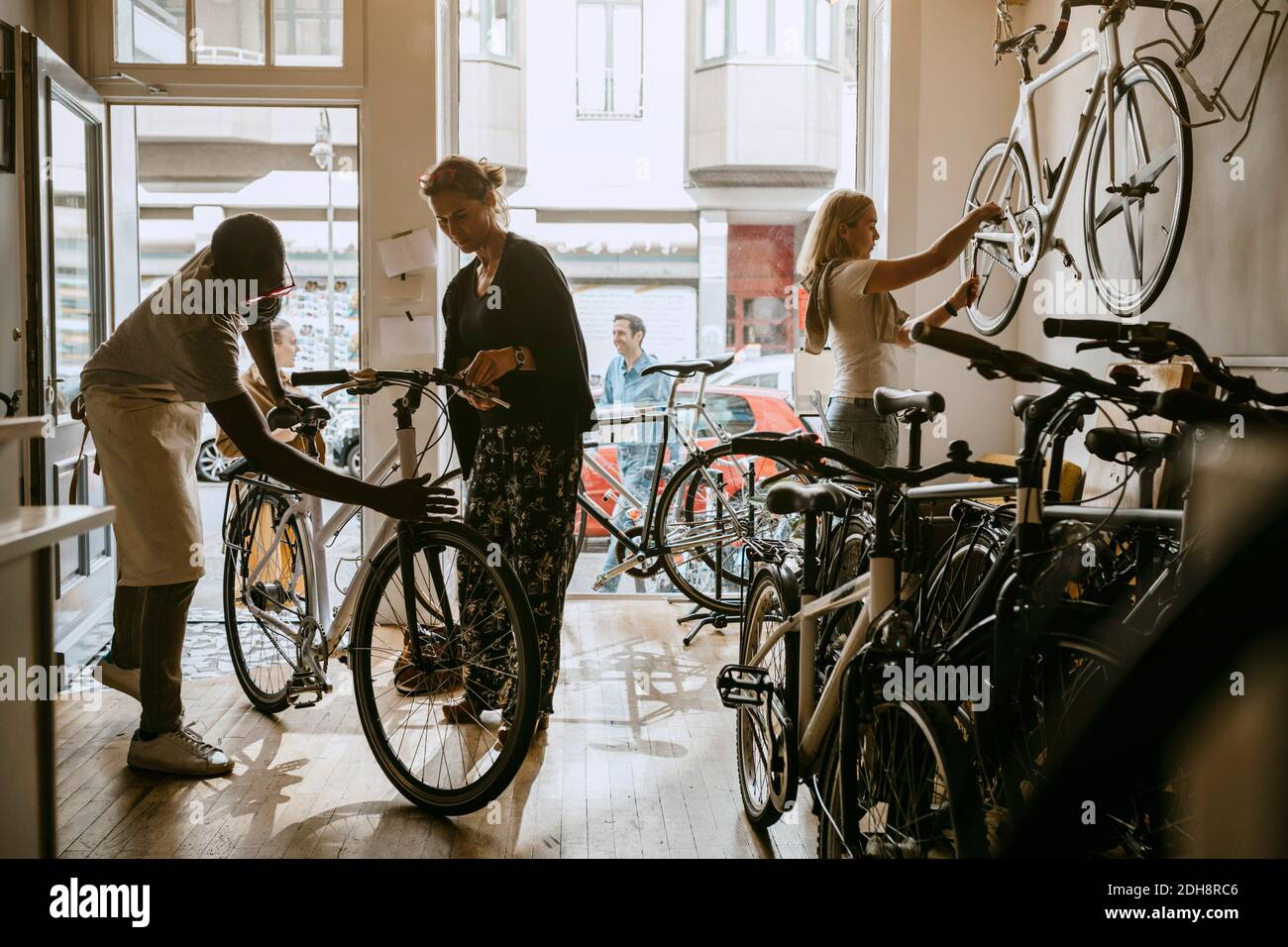 Männlicher Besitzer Reparatur Fahrrad von älteren Kunden während Kollegen arbeiten Auf dem Fahrrad in der Werkstatt Stockfoto