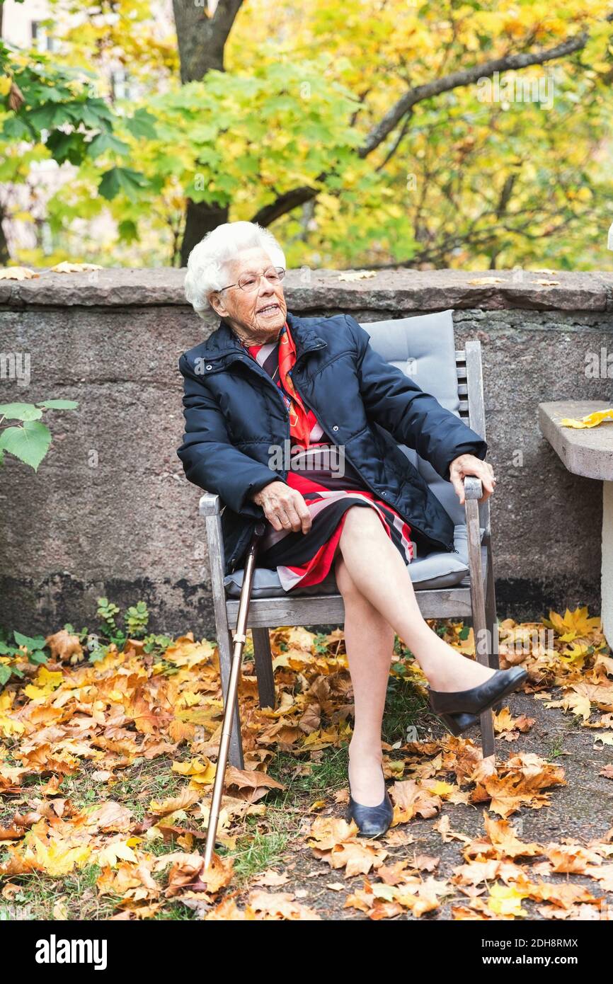 Die ganze Länge der älteren Frau sitzt auf einem Stuhl im Park Stockfoto