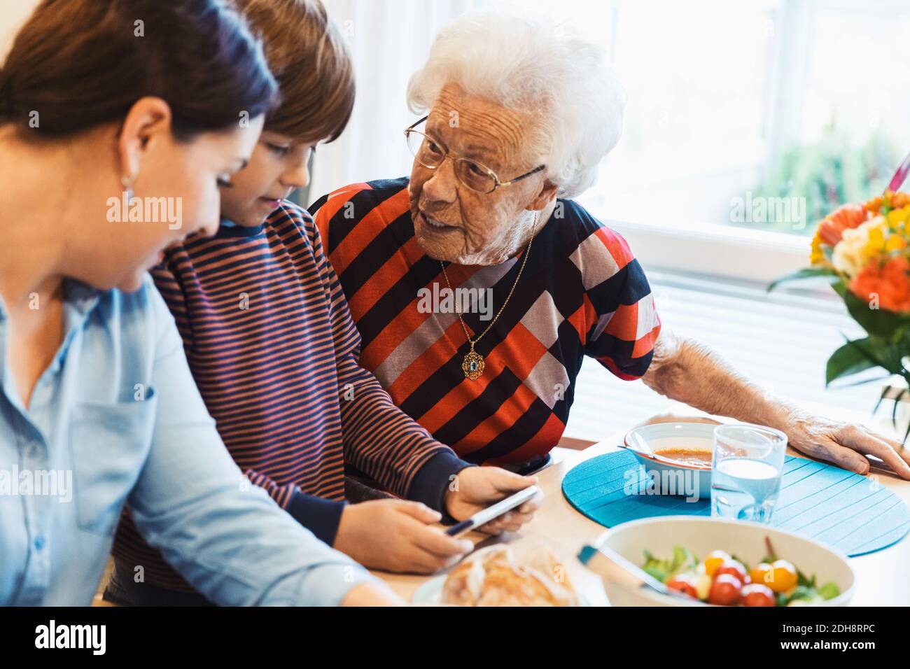 Urgroßmutter und Mutter betrachten Jungen mit Handy Im Haus Stockfoto