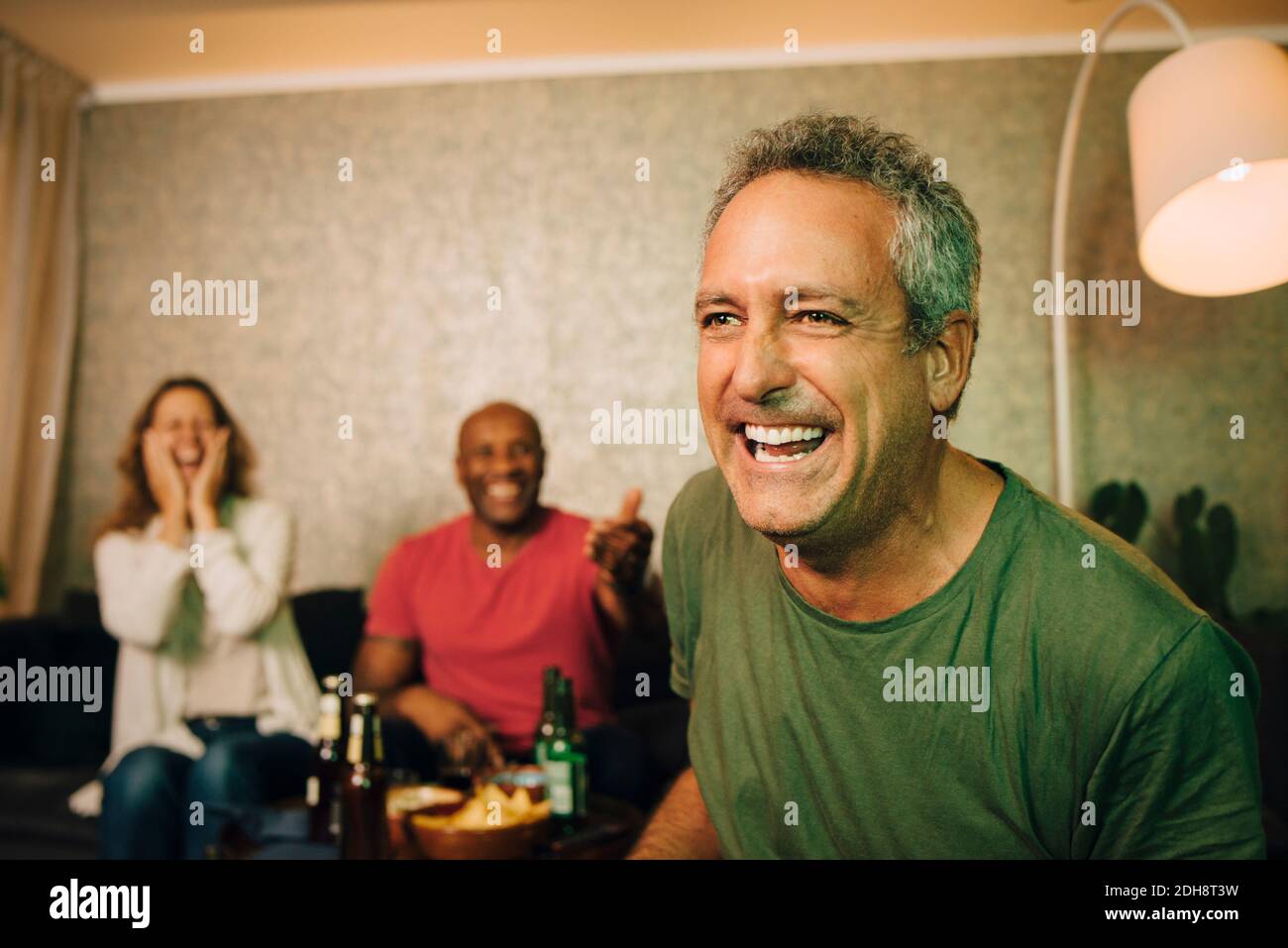 Fröhlicher Mann, der mit Freunden sitzt und zu Hause Sport beobachtet Stockfoto