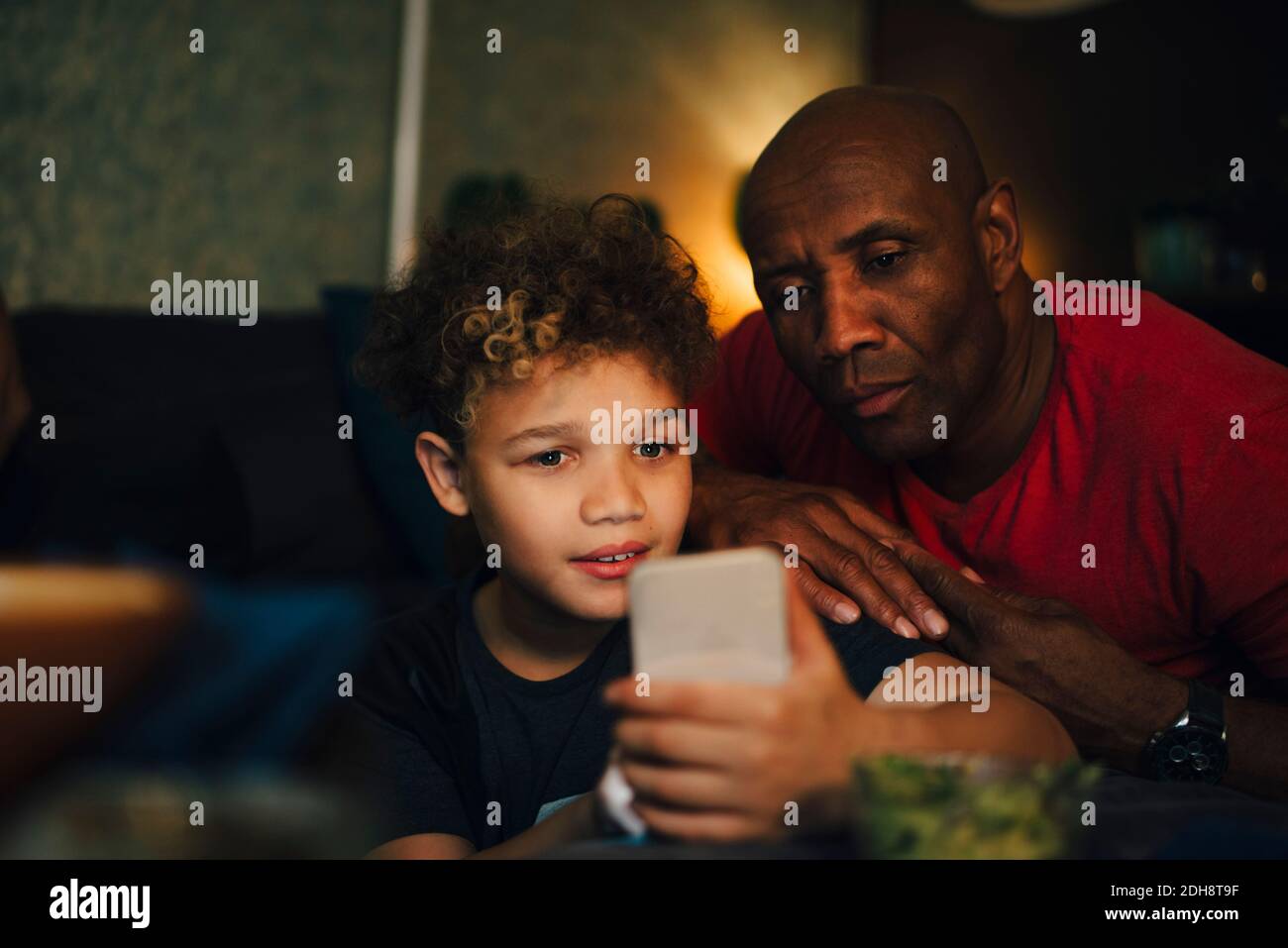 Junge mit Handy von Vater im Wohnzimmer bei Nacht Stockfoto