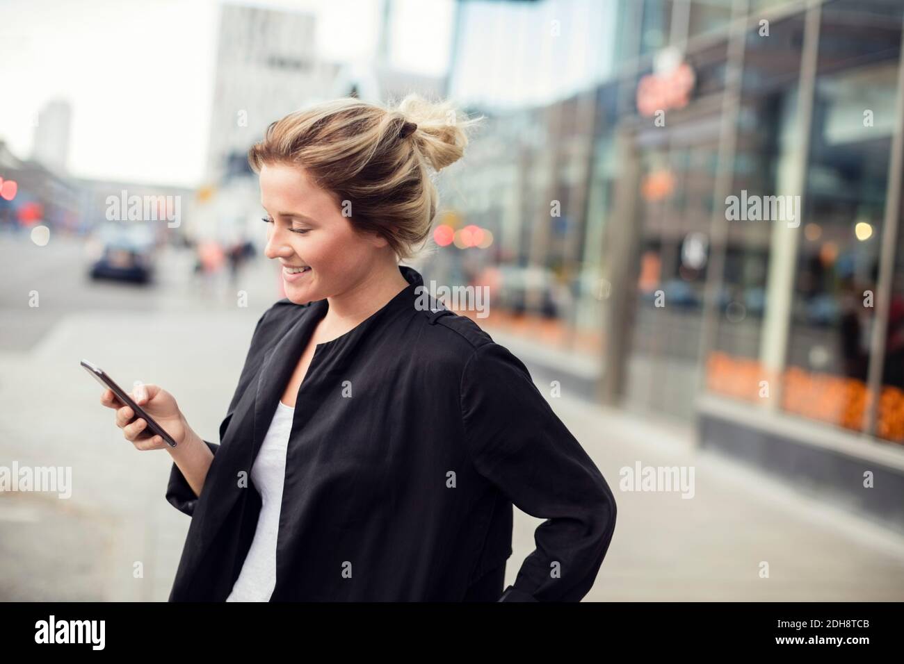 Glückliche Frau hält Handy, während sie in der Stadt steht Stockfoto