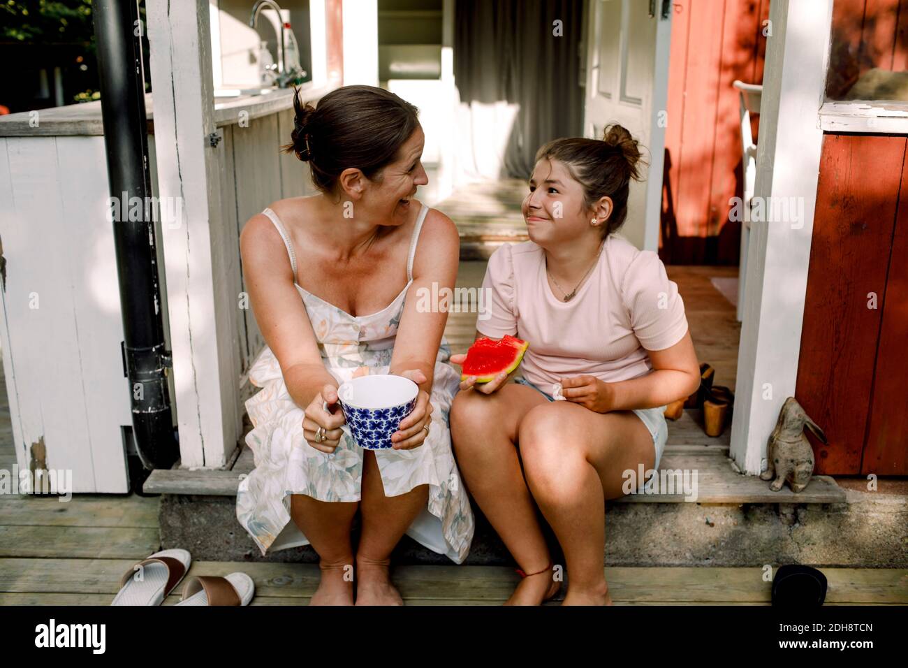 Fröhliche Mutter im Gespräch mit Tochter essen Stück Wassermelone im Freien Stockfoto