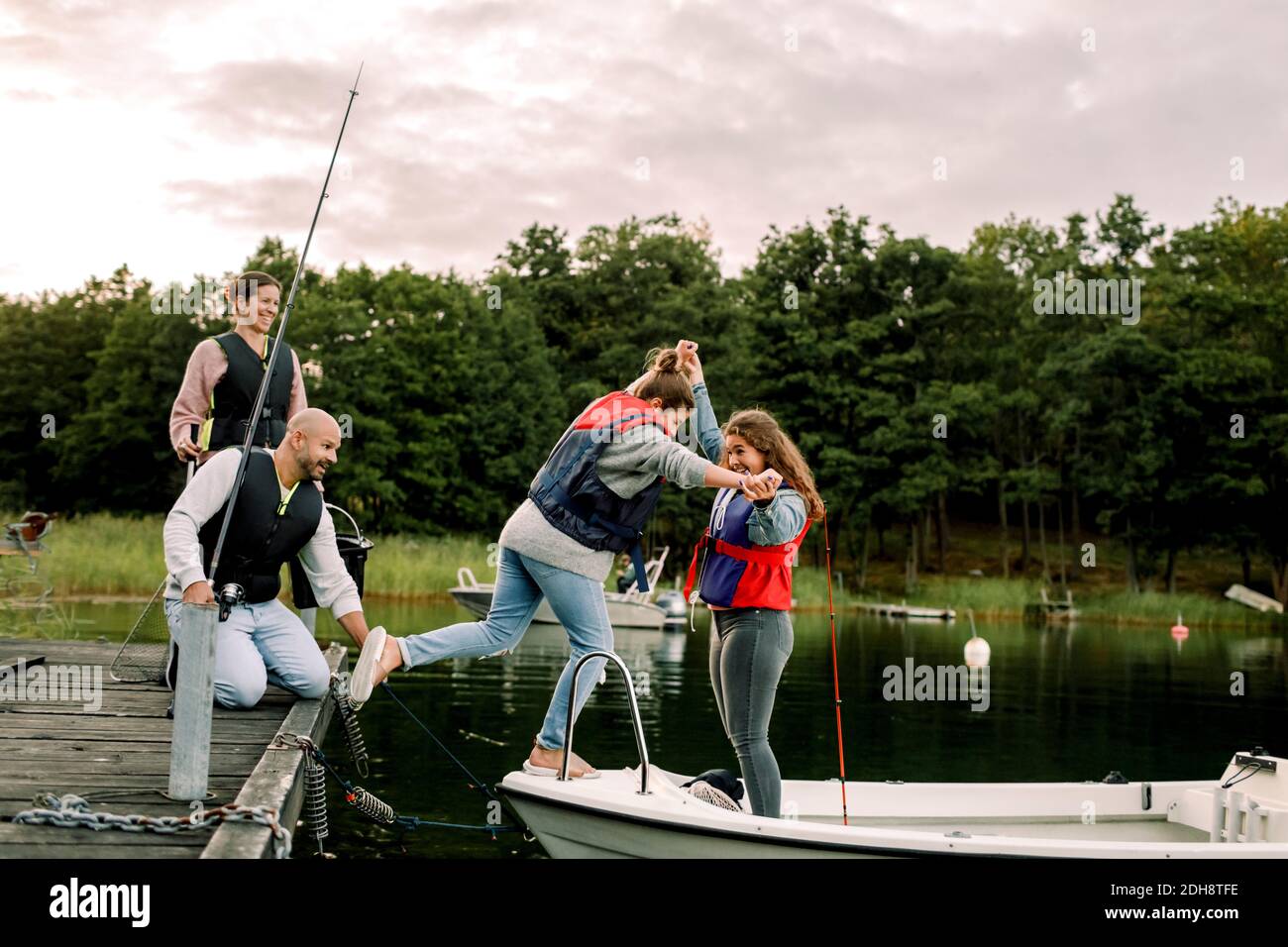 Eltern schauen auf lächelnde Tochter, die die Hand der Schwester hält, während sie stehen Im Boot über den See Stockfoto
