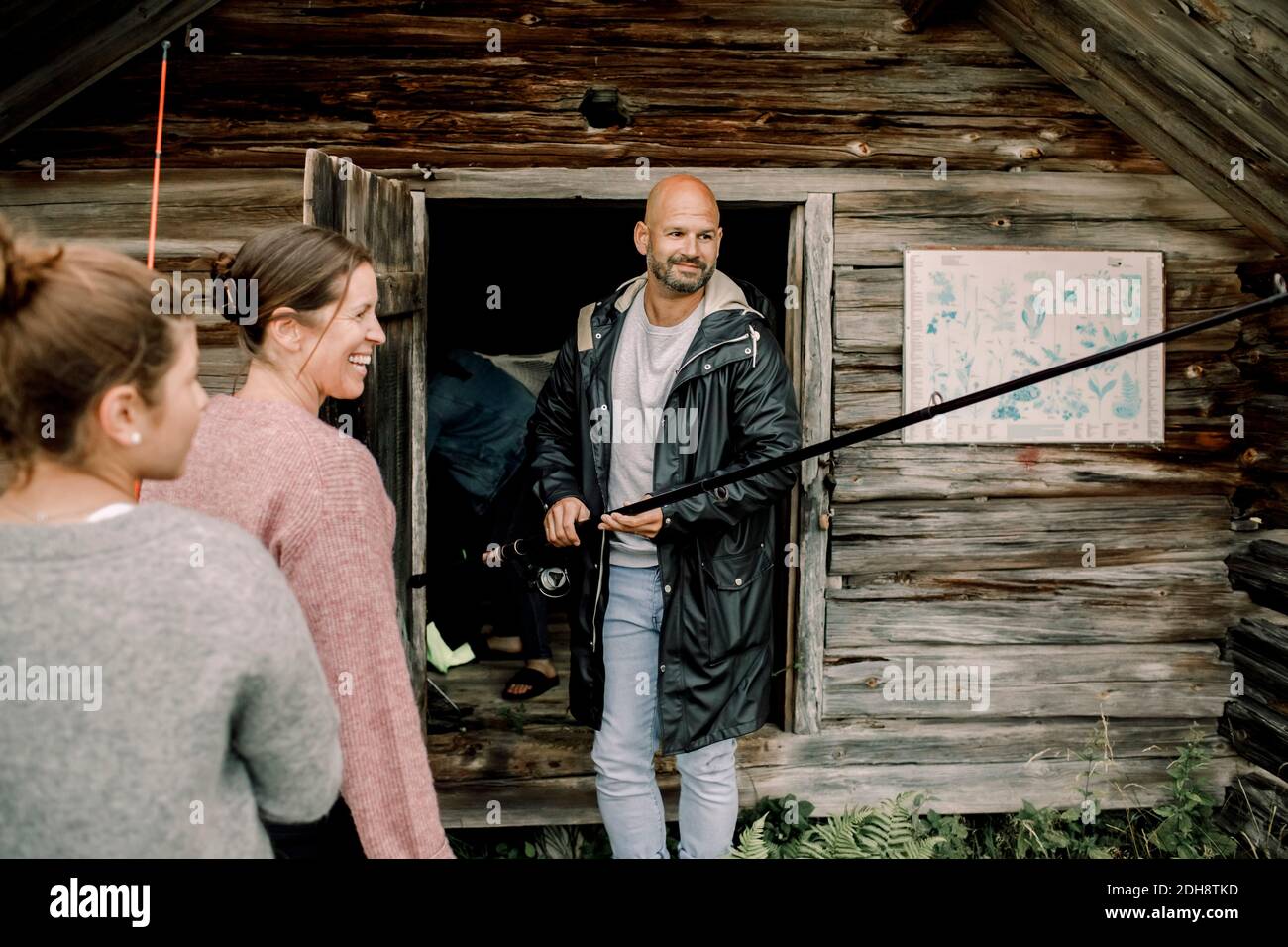 Lächelnder Vater hält Angelrute von Familie in der Nähe von Holzhaus Im Sommer Stockfoto