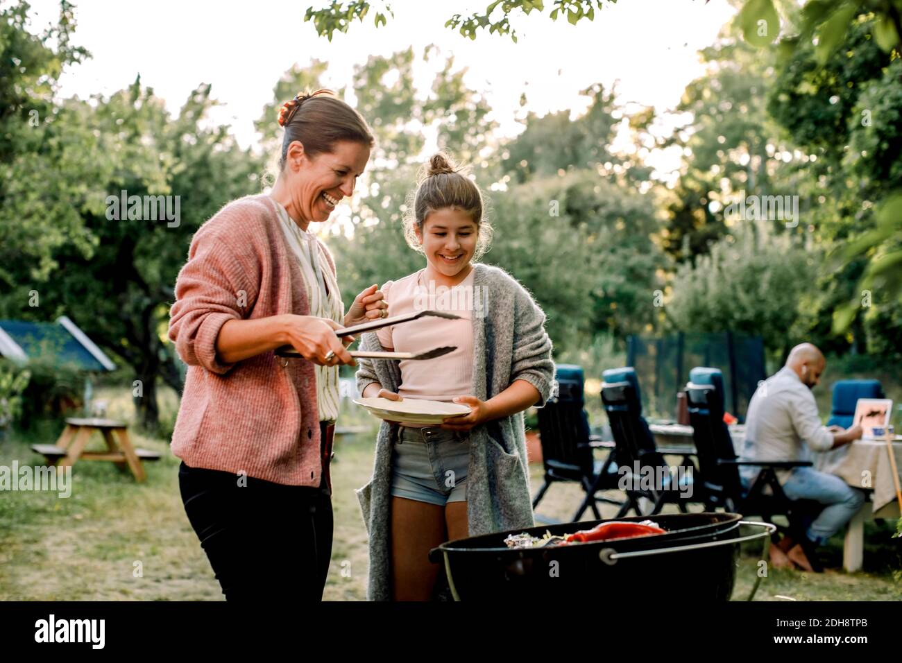 Lächelnde Mutter und Tochter, die rote Chilischote drüben betrachten Grill im Hof Stockfoto