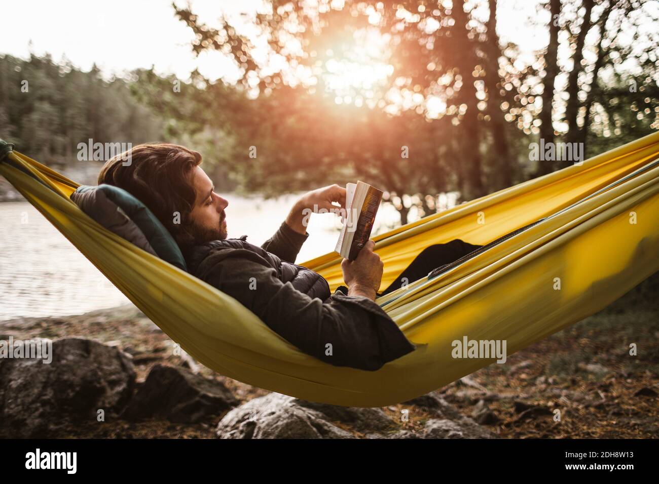 Betrachtend Mann, Buch zu lesen, während er unten über Hängematte innen liegt Wald Stockfoto
