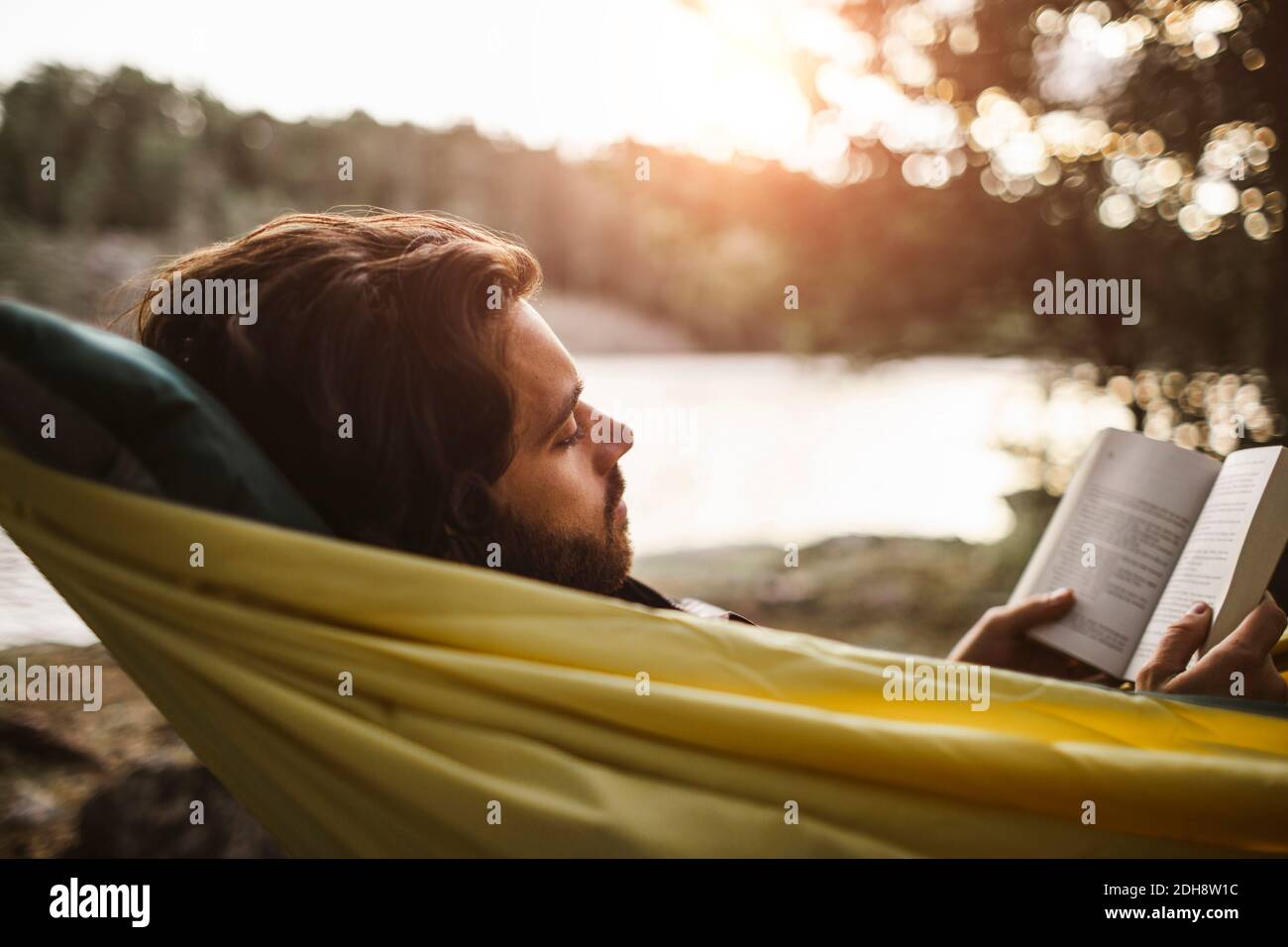 Betrachtend Mann Buch beim Liegen über Hängematte im Wald lesend Stockfoto