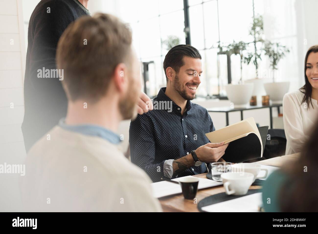 Glücklicher Geschäftsmann beim Lesen Dokument, während er mit Kollegen am Tisch sitzt Im Büro Stockfoto