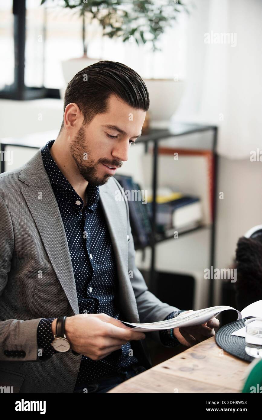 Geschäftsmann liest Dokument, während er am Tisch im Büro sitzt Stockfoto