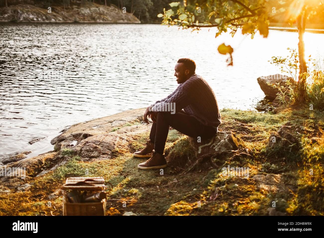 Seitenansicht des lächelnden Mannes, der am See im Wald sitzt Stockfoto