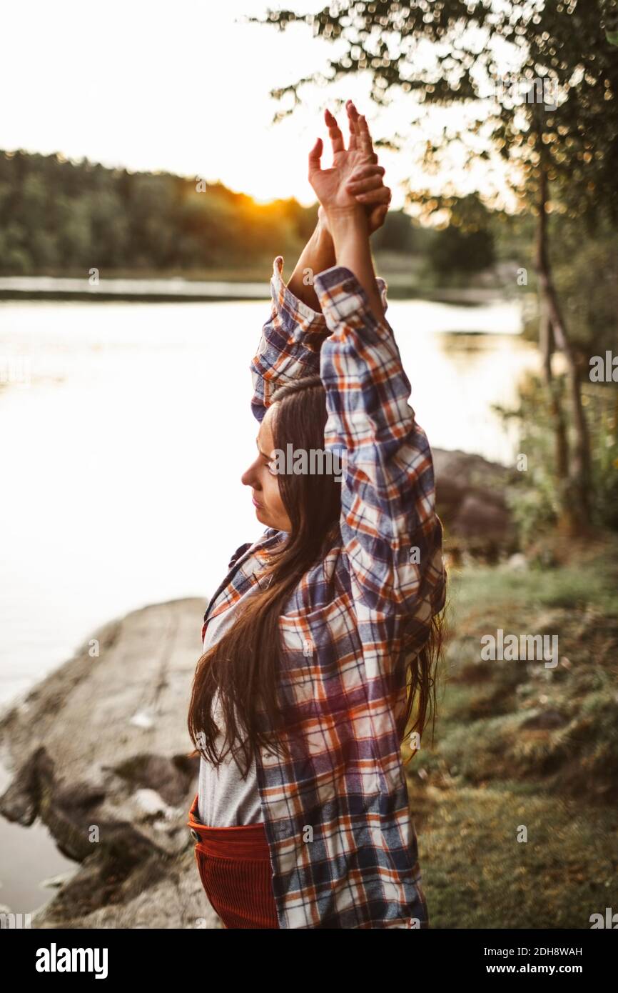 Seitenansicht einer Frau, die sich im Wald gegen den See streckt Stockfoto