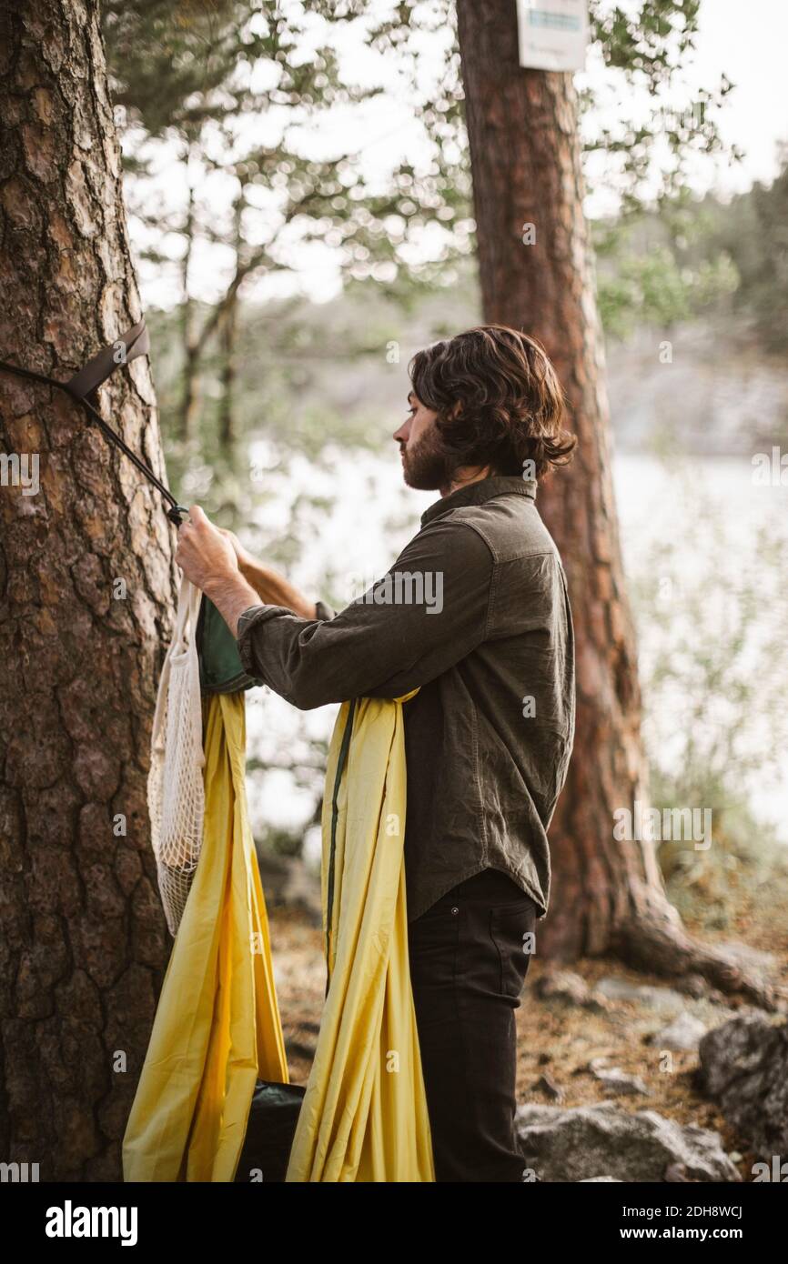 Seitenansicht des Mannes hängende Hängematte auf Baumstamm innen Wald Stockfoto