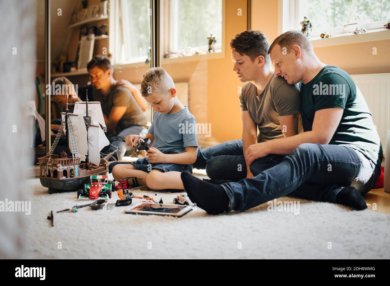 Homosexuelle Väter Blick auf Sohn spielen während der Herstellung Spielzeug Boot Zu Hause Stockfoto