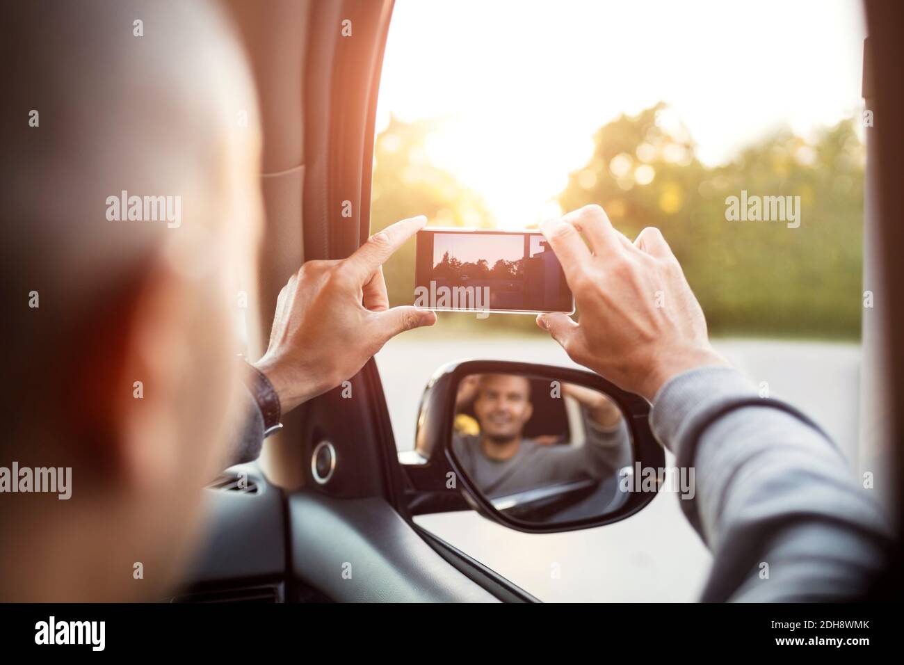 Rückansicht des Menschen beim Fotografieren vom Mobiltelefon mit Spiegelung Im Seitenspiegel Stockfoto