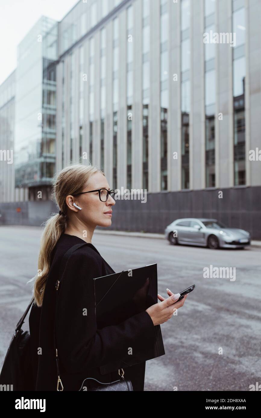 Seitenansicht einer Geschäftsfrau mit in-Ear-Kopfhörern, die die Datei in der Hand halten Stadt Stockfoto