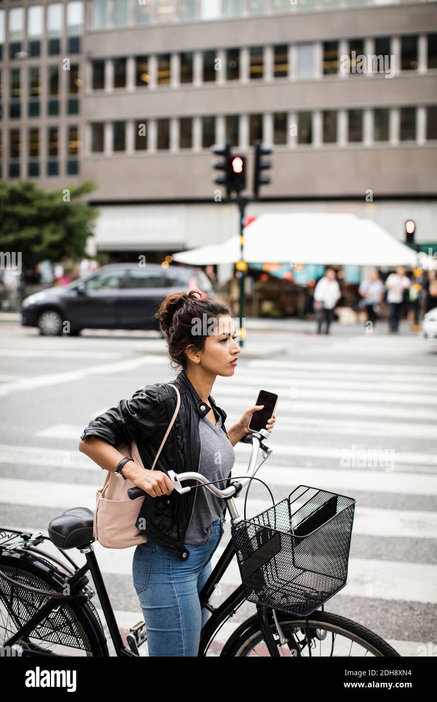 Seitenansicht einer Frau mit Fahrrad, das Telefon im Stehen hält Auf Zebrastreifen in der Stadt Stockfoto