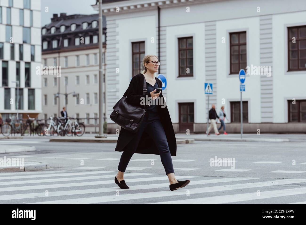 Erwägen Geschäftsfrau mit Smartphone Überquerung Straße in der Stadt Stockfoto