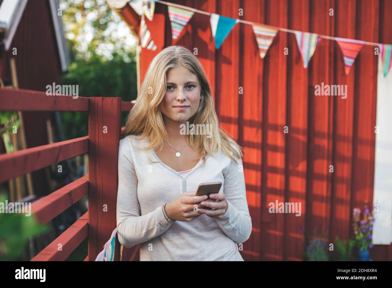 Portrait von Teenager-Mädchen mit Handy gegen Haus in Hinterhof Stockfoto