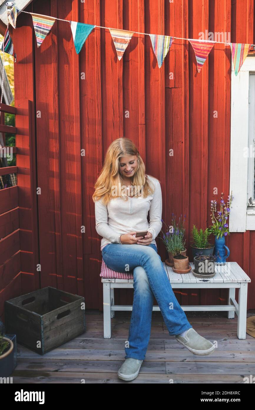 Glückliche Teenager-Mädchen mit Handy, während auf der Bank sitzen Im Hinterhof Stockfoto
