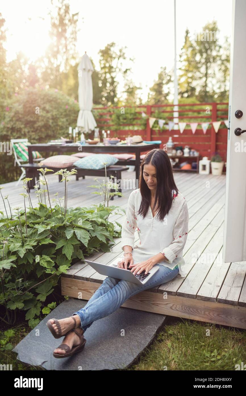 Frau mit Laptop, während sie auf dem Boden auf der Terrasse sitzt Hinterhof Stockfoto