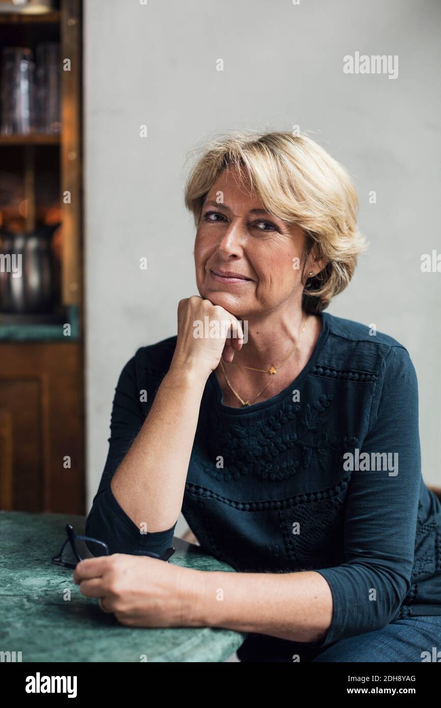 Porträt von selbstbewussten reifen Geschäftsfrau mit Hand auf Kette sitzen Am Restauranttisch Stockfoto