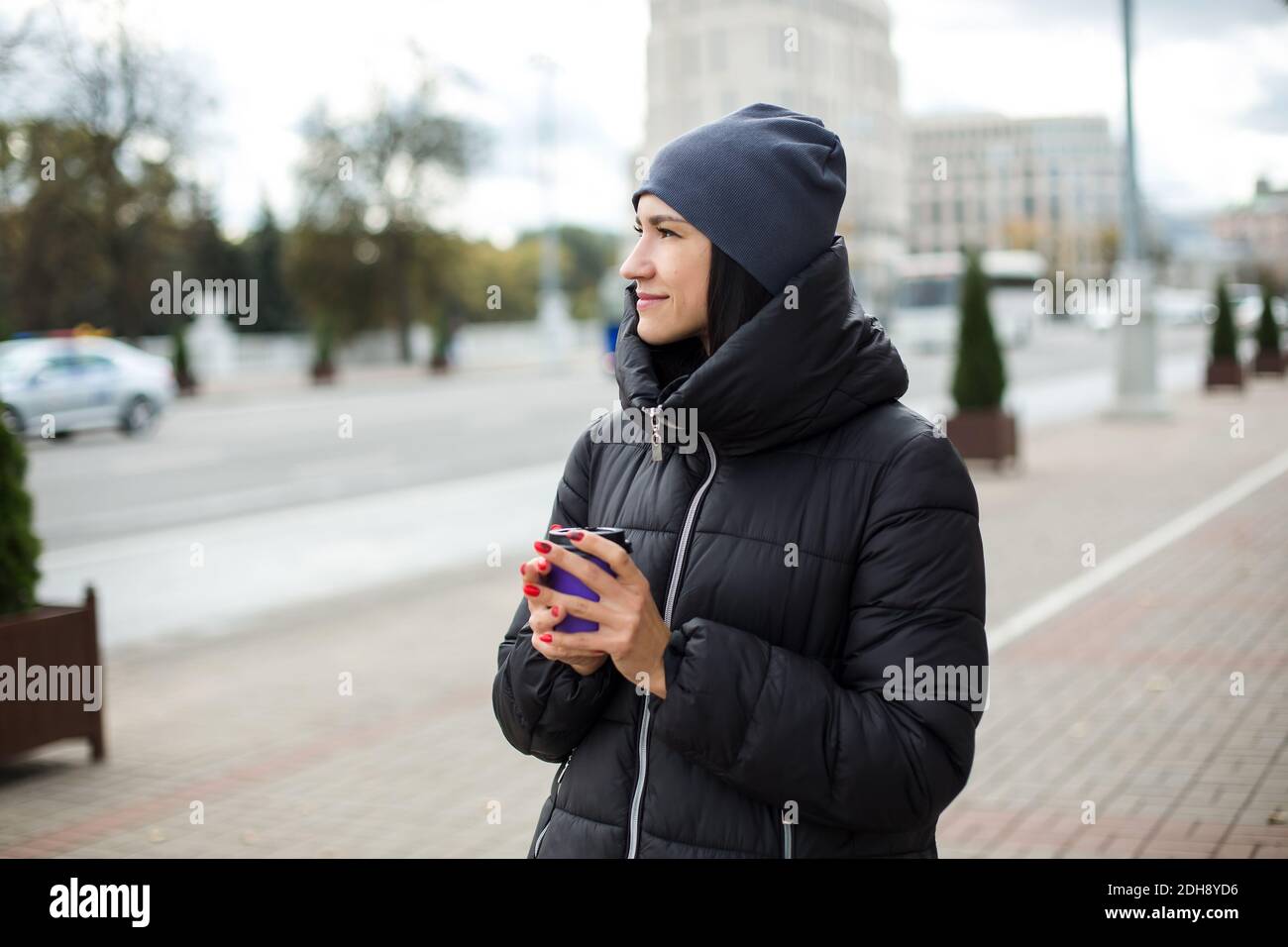Mädchen in Jacke und Hut geht mit einem Glas durch die Stadt. Stockfoto