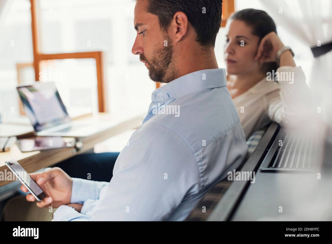 Seitenansicht eines mittelerwachsenen Geschäftsmannes, der ein Mobiltelefon benutzt Weibliche Kollegin im Büro Stockfoto