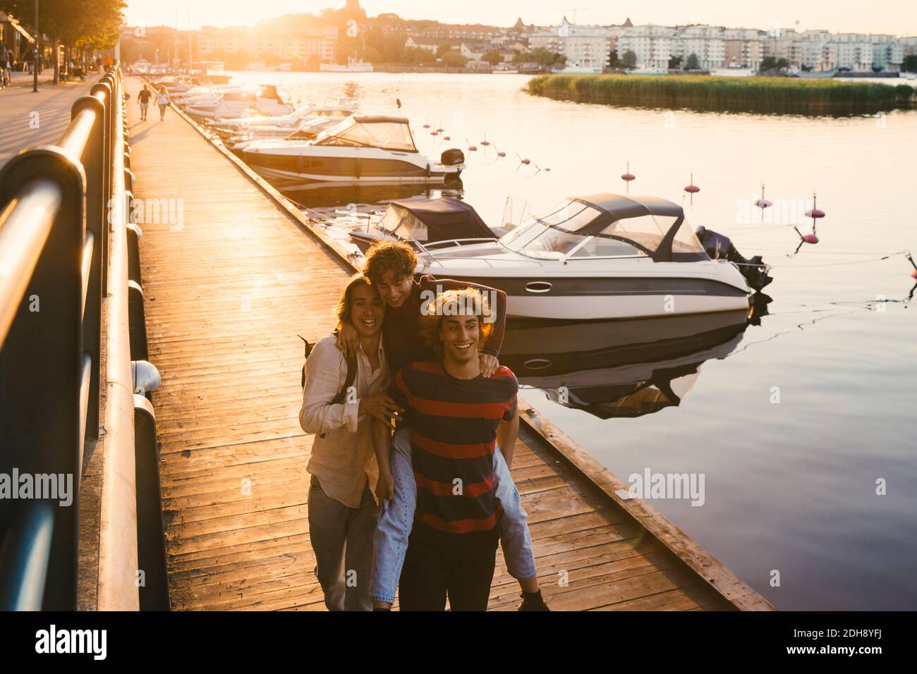 Lächelnder junger Mann gibt Huckepack Fahrt zu männlichen Freund an Hafen Stockfoto